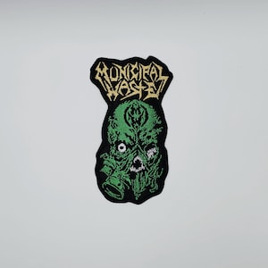 Op de afbeelding: Geborduurde patch met een groen, grotesk wezen en de gouden tekst "MUNICIPAL WASTE". De patch heeft een zwarte rand en een ongewone vorm. Ideaal voor het aanpassen van kleding of tassen.
