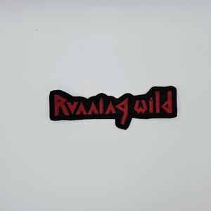 May include: Black embroidered patch with the words "Running Wild" in red, stylized lettering. The patch has a black border and is set against a white background. The text is the primary focus.
