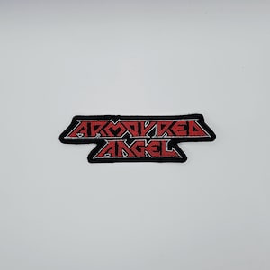 Può includere: Una toppa ricamata nera con la scritta rossa "ARMORED ANGEL". La toppa ha un bordo nero ed è probabilmente progettata per essere cucita o stirata su vestiti o accessori.