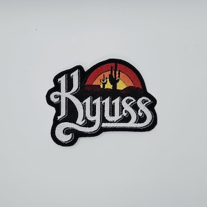 May include: Embroidered patch featuring the word "Kyuss" in white script. The patch has a black background with a desert scene in the upper portion, including a cactus and a sunset with orange, yellow, and red hues.