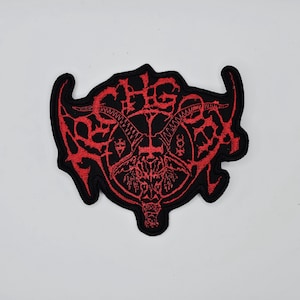 May include: Embroidered patch featuring a red and black design. The patch has a central image of a horned skull with a pentagram and other symbols. The outer edge is black, and the design is in red. The patch is likely for clothing or accessories.
