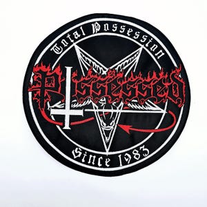 May include: Black round patch with white border featuring the text "Total Possession" and "Since 1983". The word "Possessed" is in red, stylized lettering above a white pentagram with a red arrow. A white cross is also present.
