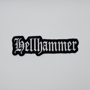 Op de afbeelding: Zwart en wit geborduurde patch met het woord "Hellhammer" in een gotisch lettertype. De patch heeft een zwarte rand en is rechthoekig. De tekst is wit.
