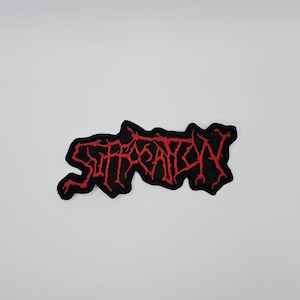 Può includere: Toppa nera ricamata con la scritta "SUFFOCATION" in rosso, con lettering gotico stilizzato. La toppa ha un bordo nero ed è probabilmente per una giacca o una borsa, che rappresenta una band o un marchio.