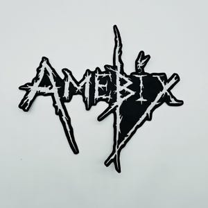 以下が含まれることがあります： AMEBIXという文字がギザギザとしたダメージ加工のフォントで刺繍された、黒と白のワッペン。黒い布地の上に白い糸で縫い付けられた文字は、鋭く使い古されたような外観で、コントラストの強いグラフィックデザインに仕上がっています。