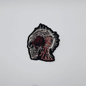 Puede incluir: Parche bordado con un diseño de calavera y una corona de espinas. La calavera es negra con detalles rojos y blancos. El parche tiene un borde negro, ideal para ropa o accesorios.