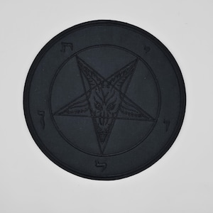 Può includere: Una toppa nera e circolare con un design a pentagramma in rilievo, raffigurante una testa di capra all'interno di un cerchio. La toppa ha una superficie strutturata e una finitura scura e opaca.