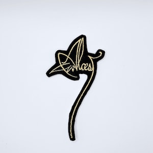 May include: Black and gold embroidered patch with the word "Arches" in a cursive font. The patch has a leaf-like shape with a long, curved stem. The embroidery is gold on a black background.
