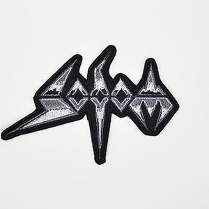 Puede incluir: Parche bordado con la palabra "SODOM" en una fuente angular estilizada. El parche tiene un borde negro y un diseño blanco y gris. Probablemente está destinado a ser aplicado en ropa o accesorios.