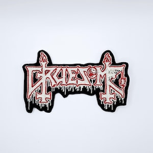 May include: Embroidered patch with the word "KREATOR" in white, outlined in red, on a black background. The design includes dripping effects and candle-like shapes at each end. The patch is rectangular.