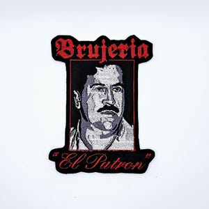 May include: Embroidered patch featuring a portrait of a man with a mustache, framed in black with red text. The text at the top reads "Brujeria" and the text at the bottom reads "El Patron".