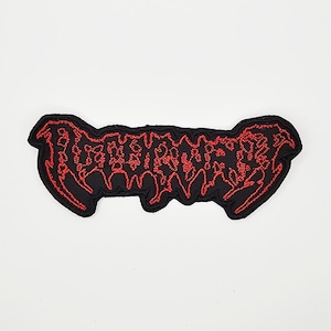 May include: A black embroidered patch with red stitching. The patch features stylized text in a gothic font. The patch has a black border and is set against a white background. The patch is likely for clothing or accessories.