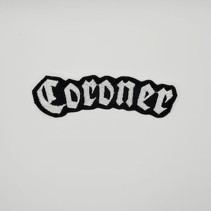 May include: A black embroidered patch featuring the word Coroner in white gothic-style lettering. The patch has a curved shape that follows the contour of the text, with a thick black border surrounding the white stitched letters throughout.