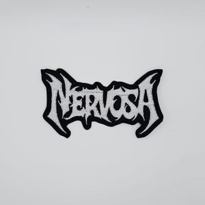 Puede incluir: Un parche bordado en blanco y negro con la palabra "Nervosa" en una fuente gótica estilizada. El parche tiene un borde negro y está diseñado para ser cosido o planchado en ropa o accesorios.