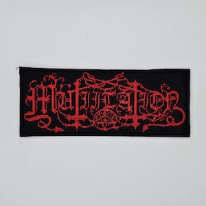 May include: Black rectangular patch with the word "Matador" embroidered in red, gothic-style lettering. The design includes ornate flourishes and a circular emblem. The patch is likely for clothing or accessories.