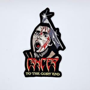 May include: Embroidered patch featuring a screaming face with blood and a blade. The patch has the word "CANCER" in red and yellow, and "TO THE GORY END" in yellow. The patch is black with white and gray details.