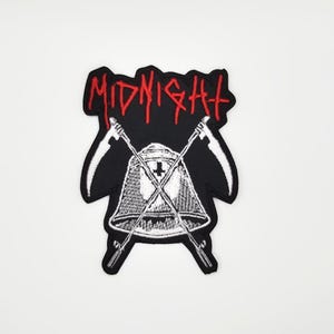 Puede incluir: Parche negro con la palabra "MIDNIGHT" en letras rojas estilizadas. El parche presenta un casco blanco con una cruz y dos hoces cruzadas. El parche es un emblema.