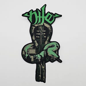 Op de afbeelding: Geborduurde patch met een gestileerd cobra-ontwerp en het woord "Nile" in groen, op een zwart-groen camouflagepatroon. De patch heeft een gedetailleerd ontwerp met een slang die zich rond een centraal element wikkelt.