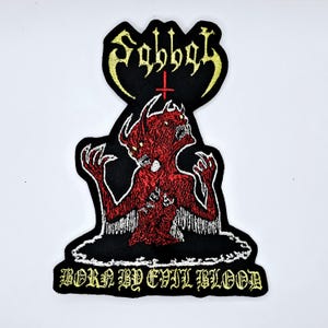 May include: Embroidered patch featuring the word "Sabbat" in yellow, above a red demon with two heads and outstretched arms. The text "BORN BY EVIL BLOOD" is below the demon, all on a black background.