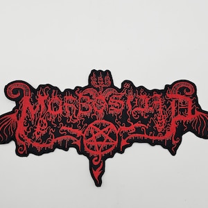Puede incluir: Parche negro con la palabra "Morbid" en rojo, con una fuente gótica y diseños intrincados. El parche presenta un pentagrama y otros elementos decorativos.