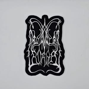 Peut inclure: Écusson brodé noir avec texte blanc et un motif stylisé. Le patch présente un design unique et symétrique avec des lignes et des courbes complexes. Le texte semble être un nom de groupe ou un logo.