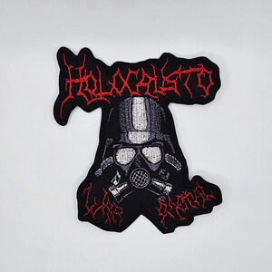 Può includere: Toppa ricamata nera con un disegno di maschera antigas e la scritta "HOLOCAUSTO" in lettere rosse stilizzate. La toppa ha un bordo frastagliato ed è destinata all'abbigliamento o agli accessori.
