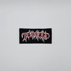 May include: Black rectangular patch with the word "TANKERD" embroidered in red and white. The lettering has a gothic, stylized design. The patch is likely for clothing or accessories.