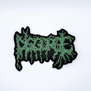 May include: Black embroidered patch with the word "DECAY" in a green, stylized, and distressed font. The patch has a jagged, irregular shape and is likely for clothing or accessories.