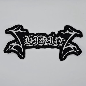 Peut inclure: Écusson brodé noir avec lettrage gothique blanc. Le patch a une forme de bannière avec des accents blancs décoratifs sur les bords. Le texte est stylisé et semble être un nom de groupe ou de marque.