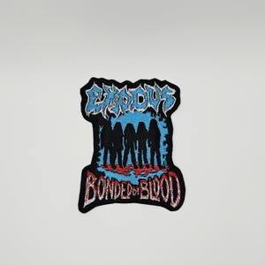 May include: An embroidered patch featuring the text EXODUS in light blue at the top and BONDED BY BLOOD in red at the bottom. The centre displays five black silhouettes of figures standing against a light blue background with red accents.