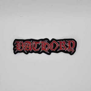 May include: Black embroidered patch with the word "BATHORY" in red gothic lettering. The patch has a silver border and is rectangular in shape. The patch is likely for a jacket or bag.