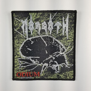 Puede incluir: Un parche bordado negro y verde con el nombre de la banda "MORGOTTH" en letras plateadas con purpurina. El parche presenta un insecto negro y plateado con la palabra "ODIUM" en letras rojas debajo. El parche está rodeado por un borde negro.