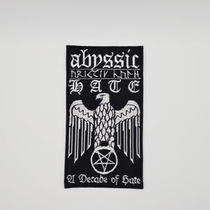 May include: Black and white embroidered patch featuring the word "abyssic" in gothic lettering above the word "HATE". A white eagle with a pentagram is centered below the text. The phrase "21 Decade of Hate" is at the bottom.
