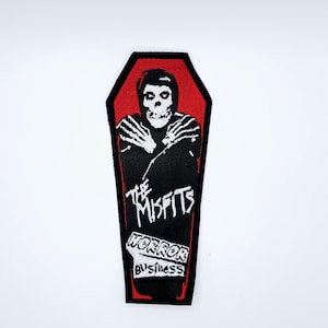 Può includere: Toppa nera e rossa con un design a bara. Presenta una figura scheletrica e il testo "The Misfits Horror Business". La toppa ha un bordo nero ed è progettata per abbigliamento o accessori.