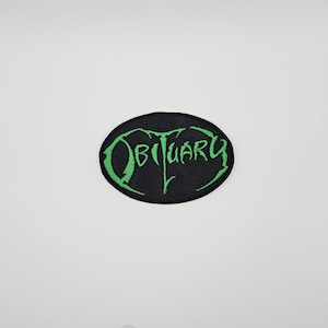 May include: Black oval patch featuring the word "OBITUARY" in green, stylized lettering. The patch has a green border and is set against a white background. The text appears to be embroidered.