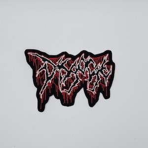 May include: A black patch with the word "DEATH" in a stylized, dripping font. The text is outlined in white and filled with a red, blood-like design. The patch has a black border.