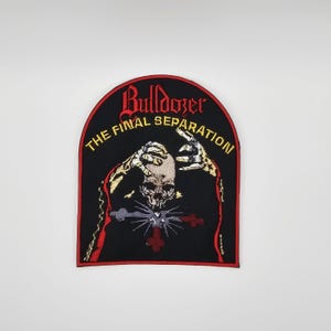 Pode incluir: Patch bordado com fundo preto e borda arqueada vermelha. O patch apresenta a palavra "Bulldozer" em escrita vermelha acima das palavras "The Final Separation" em amarelo. Uma caveira com mãos esqueléticas está no centro.
