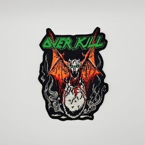 May include: An embroidered patch featuring the text OVER KILL in bright green letters above a graphic of a winged creature emerging from a cracked egg. The creature has orange wings, a white skull-like head, and green eyes on a black background.