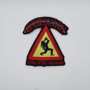 May include: Embroidered patch with the word "GEHENNAH" in red, arched above a yellow triangle with a black border. Inside the triangle is a black silhouette of a person holding a bottle. The text "King of the sidewalk" is below the triangle.