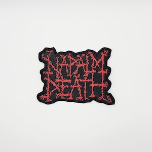 Puede incluir: Parche negro bordado con el texto "NAPALM DEATH" en rojo, con letras estilizadas. El parche tiene un borde irregular y dentado. Un diseño audaz.
