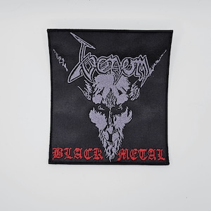 May include: Black square patch with the word "Venom" in a stylized font above a skull graphic. The words "BLACK METAL" are embroidered in red at the bottom. The patch is likely for a jacket or bag.