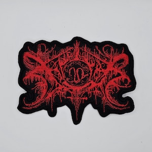 May include: A black embroidered patch with a red, intricate design. The patch features a central circular emblem with a stylized 'W' shape, surrounded by ornate, abstract patterns. The edges are jagged, and the overall aesthetic is gothic.
