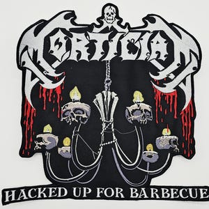 May include: A black embroidered patch featuring the white text MORTICIAN at the top with a small skull above it. Below, a chandelier holds five skulls with yellow flames, surrounded by red blood drips. The bottom text reads HACKED UP FOR BARBECUE.
