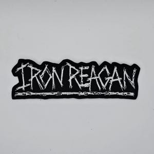 Peut inclure: Écusson brodé noir avec le texte blanc « IRON REAGAN ». Le patch a un bord dentelé et une ligne de couture blanche en bas. Le patch rectangulaire est conçu pour être appliqué sur des vêtements ou des accessoires.