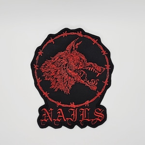 May include: Embroidered patch featuring a snarling red wolf's head within a barbed wire circle on a black background. The word "NAILS" is embroidered in red gothic lettering below the circle. The patch has a black border.
