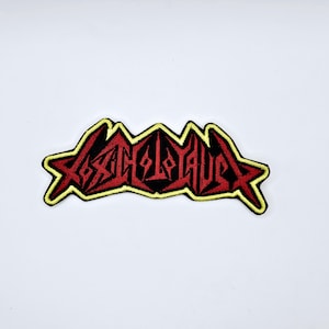 May include: Embroidered patch featuring the word "SANGUIS" in a stylized, gothic font. The text is red with black accents, outlined in yellow, and set against a black background. The patch has a star-shaped border.