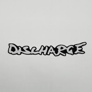 May include: A black and white embroidered patch with the word "DISCHARGE" in a stylized font. The text is in white with a black outline, and the patch has a white background.