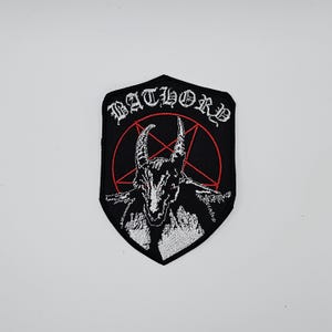 May include: Black and white embroidered patch featuring a goat-like figure with horns inside a red pentagram. The word "BATHORD" is embroidered in white above the image. The patch has a black shield shape.