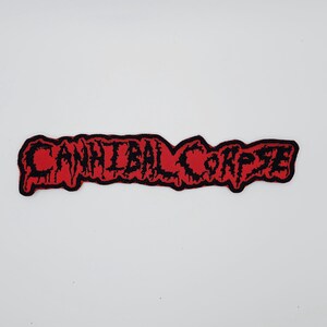 以下が含まれることがあります： 赤色の背景に黒色の「CANNIBAL CORPSE」の文字が描かれた長方形のパッチ。文字はスタイリッシュにデザインされています。黒い縁取りがあり、衣類やアクセサリーに適用することを目的としています。
