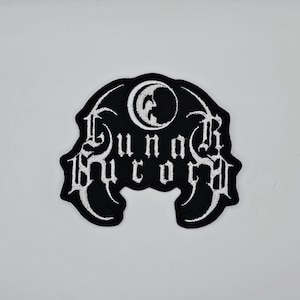 Puede incluir: Parche bordado en blanco y negro con el texto "Luna Rucor" en fuente gótica. El parche presenta un diseño de media luna en la parte superior. El parche es probablemente para ropa o accesorios.